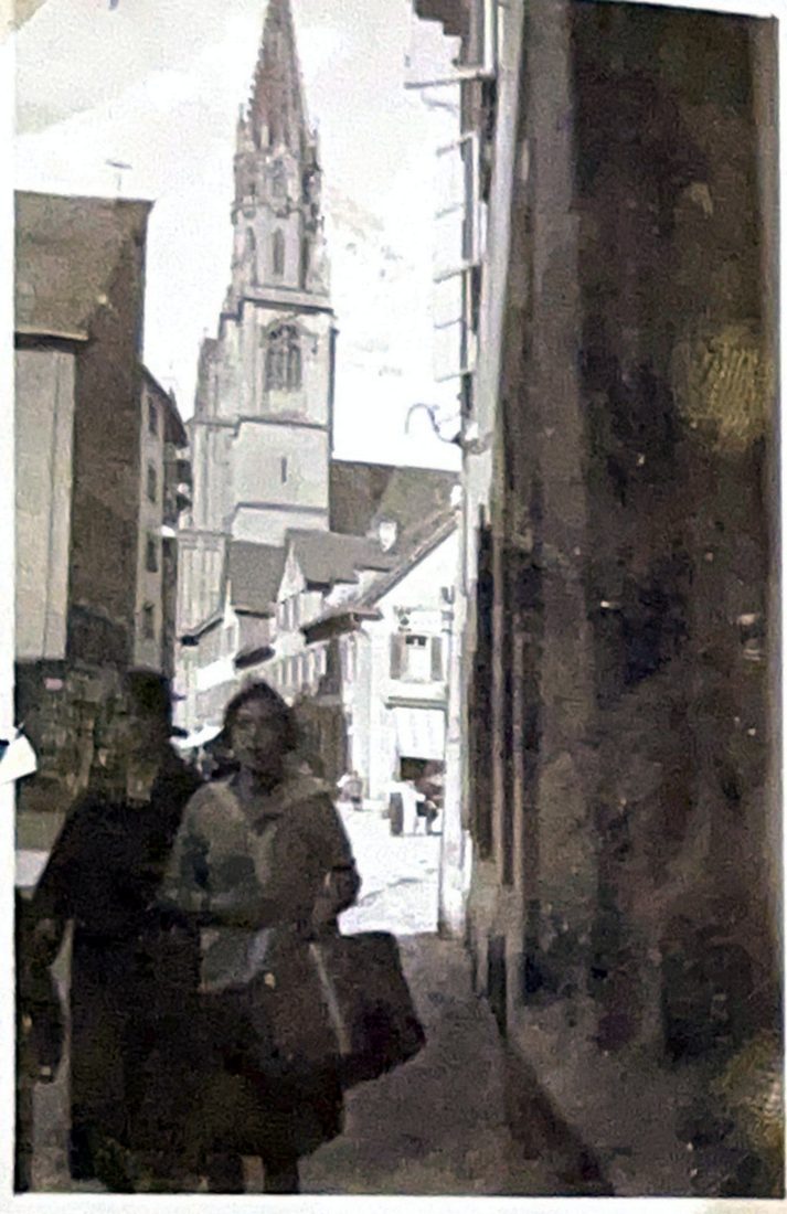 Gasse mit Fußgängern, dahinter ein Kirchturm